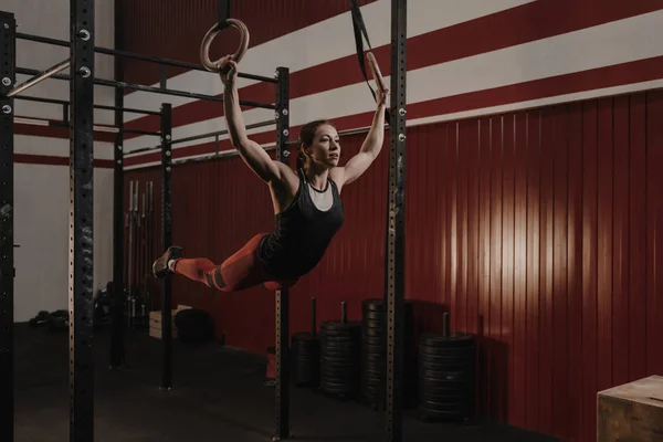 Atlet wanita muda berayun di atas ring senam di gym crossfit — Stok Foto