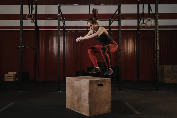 Wanita muda crossfit melakukan box jumping di gym . — Stok Foto