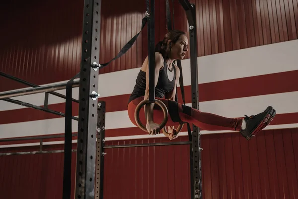 Mulher Crossfit fazendo exercícios abdominais em anéis de ginástica no ginásio — Fotografia de Stock