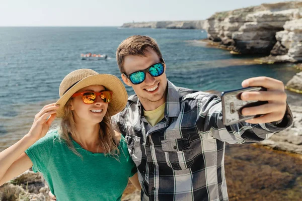 Młoda para robi selfie i uśmiecha się na malowniczym morzu i klifach — Zdjęcie stockowe