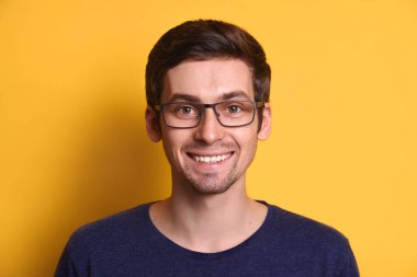 Sarı stüdyo arka planında mutlu mesut sırıtan gözlüklü, gündelik kıyafetler giyen çekici, neşeli bir adamın yakın plan portresi. Kendine güvenen, öğrenci, serbest çalışan. İnsani duygu içeriği