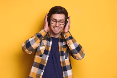 Gözlüklü, mutlu ve tasasız bir adam en sevdiği müziği kablosuz kulaklıkla dinliyor, gözleri kapalı bir melodinin ritmiyle dans ediyor, eğleniyor. Sarı arka plan. Müzik konsepti