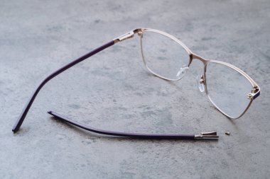 Optik masasında kırık bir tapınak bulunan düzeltici gözlüklerin yakın çekimi. Profesyonel optometri, ölçüm, gözlük imalatı, gözlükçülük atölyesindeki hasarlı gözlüklerin tamiri ve onarımı