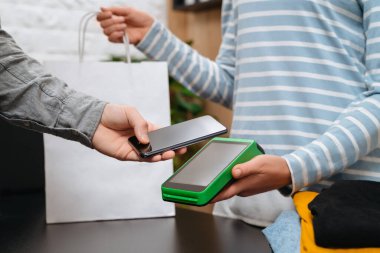 Temassız ödeme konsepti, NFC teknolojisinin yanında akıllı telefon tutan erkek müşteri işlem yapıyor, kıyafet mağazasındaki terminal kasiyerinin faturasını ödüyor. NFC teknolojisi