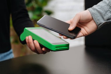 NFC terminalinin yanındaki akıllı telefonlu bir adamın eli dükkânda. Müşteri NFC terminali üzerinden ulaşılamayan ödemeler için akıllı telefon kullanıyor. Temassız ödeme ve NFC teknoloji kavramı