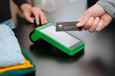 Yakından bakıldığında, NFC terminalinin giyim mağazasından alışveriş yaparken, banka kredi kartını kullanarak ulaşılamaz ödeme yaptığı görülüyor. Bağlantısız ve NFC teknoloji konsepti