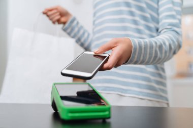 NFC teknolojisi kullanılarak akıllı telefondan satın alınan kadın müşteri. Kadının eli, temassız makine ya da NFC terminali aracılığıyla ödeme yapıyor. Temassız ödeme kavramı