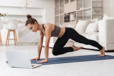 Genç formda kız evde spor yaparken dizüstü bilgisayarda özel ders izliyor. Tozluklu güzel bir atletik kız ve en iyi yoga ya da odada egzersiz yapan. Spor, sağlıklı yaşam tarzı