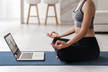 Formda kadın koçun internette hatha yoga, Sukhasana duruşu, dinlenme ve meditasyon eğitimi videosu var. Yoga eğitmeni evde sanal ders için dizüstü bilgisayar kullanıyor. Sağlıklı yaşam tarzı