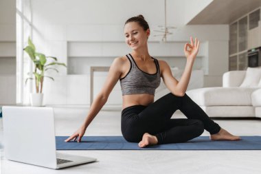 Video konferansında online ders verirken egzersiz yapan kadın yoga eğitmeni. Spor kadını oturma odasında sanal sınıf için dizüstü bilgisayar kullanarak yoga yapıyor. Sağlıklı yaşam tarzı, sağlık.