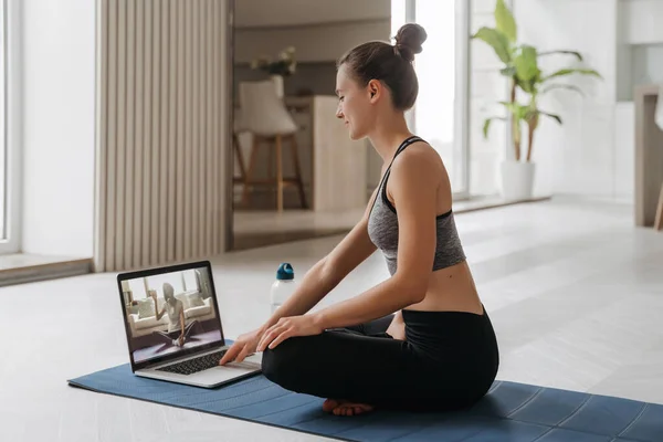 Yoga öğretmeni evde video konferansında sanal yoga dersi veriyor. Güzel, formda bir kadın oturma odasında dizüstü bilgisayarla yoga yapıyor. Spor ve spor konsepti. Çevrim içi eğitim