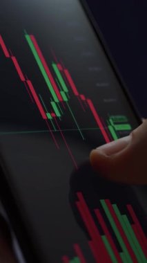 Finansal analiz ve yatırım verilerini izlemek için borsa grafikleri ile ticaret uygulamasını kullanarak akıllı telefonu elinde bulunduran tüccarı kapat. Dikey video