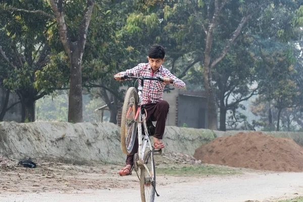 A teenager boy showing stunts with bicycle keeping front wheel in the air