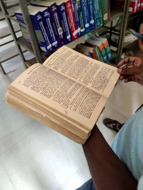 Malda, Hindistan... 12 Haziran 2019: Bir kütüphanede sarımsı sayfaları olan eski bir kitabı tutan genç bir erkek.