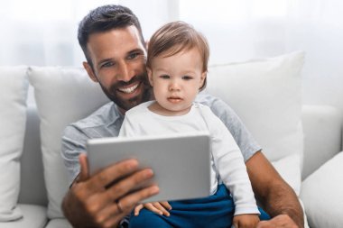 Şirin bebek oğlu tutarak ve tablet vasıl seyir yakışıklı beyaz adam.