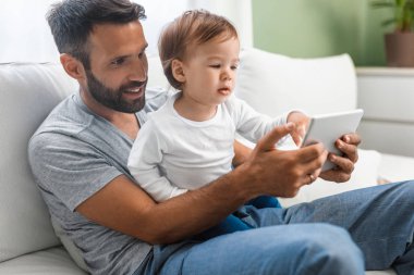Şirin bebek oğlu tutarak ve tablet vasıl seyir yakışıklı beyaz adam.