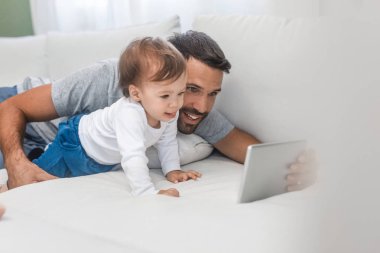 Şirin bebek oğlu tutarak ve tablet vasıl seyir yakışıklı beyaz adam.