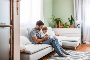 Evde oturan ve onun çocuğuna oynayan yakışıklı beyaz adam.