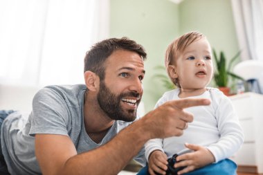 Yerde yatarken ve şirin bebek oğlu ile oynarken mutlu gülümseyen beyaz adam.