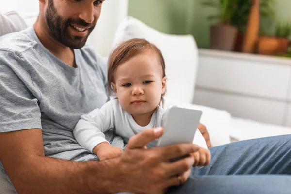 赤ちゃん息子を押しながら携帯電話を見て笑顔の白人男性 — ストック写真