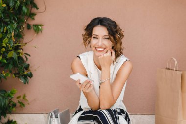 Güzel esmer cep telefonunu tutan ve kameraya bakarak gülen.