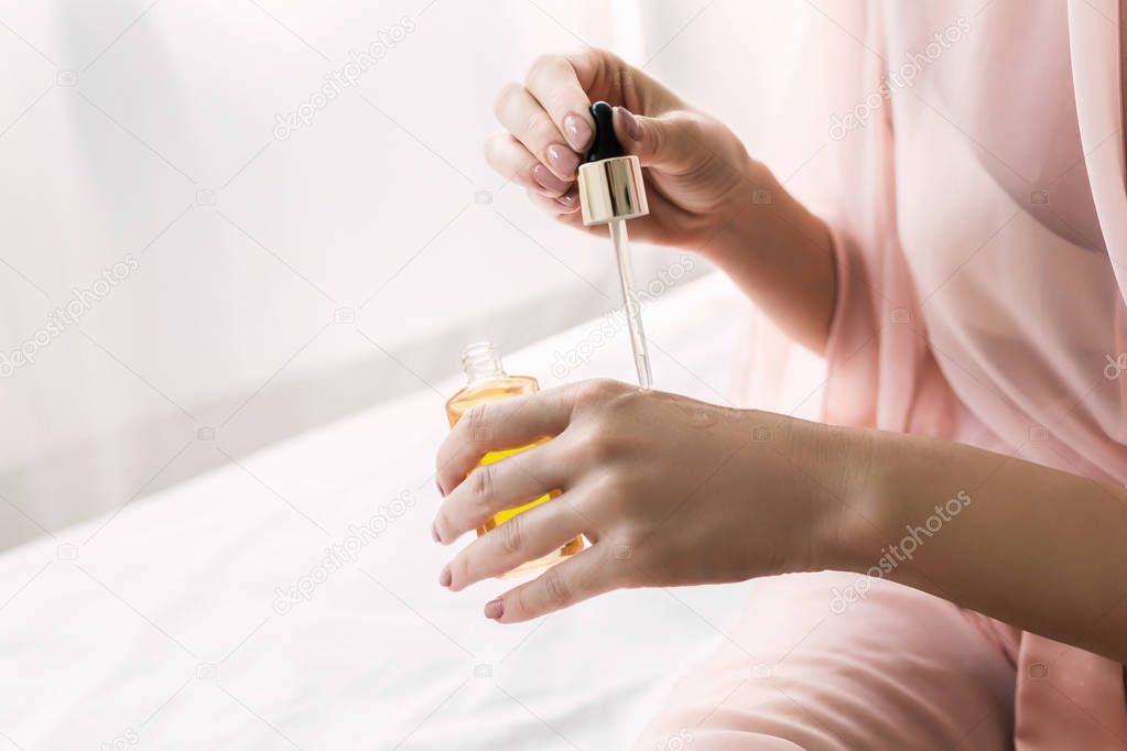 Hands of unrecognisable  woman holding bottle with cosmetic serum.