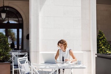 Kahve dükkanında oturmuş ve onu laptop okuma güzel gülümseyen beyaz kadın.