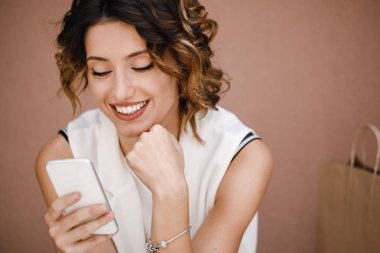 Gülümseyen güzel beyaz kadın cep telefonu üzerinde okuma.