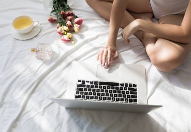 Sabahleyin yatağında oturmuş ve onu laptop yazarak unrecognisable kadın kırpılmış.