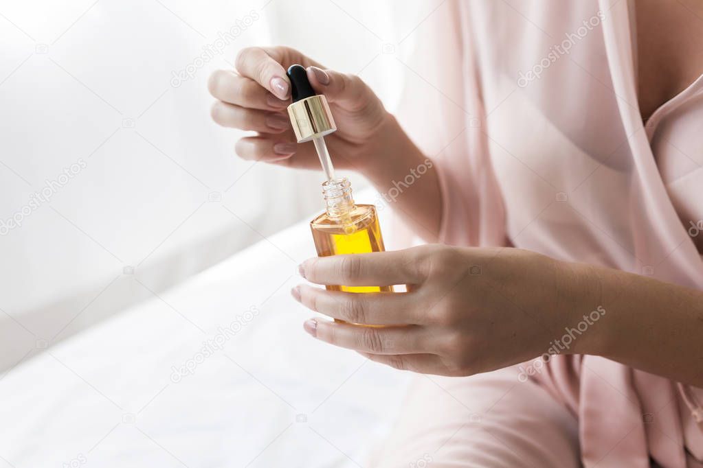 Hands of unrecognisable  woman holding bottle with cosmetic serum.