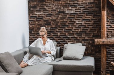 Evde kanepede oturan ve laptop arıyorum güzel sarışın gülümseyen beyaz bir kadın.