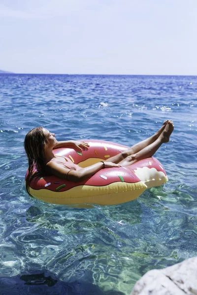 Pretty woman lying on floating ring on Mediterranean sea and enjoying sunbathe.