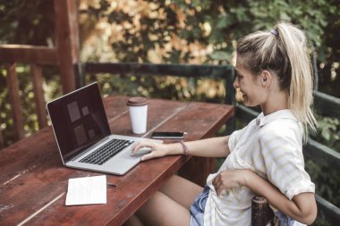Terasta oturan ve onu laptop kullanarak güzel sarışın kadın beldedir.