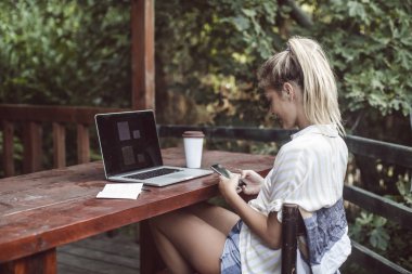 Terasta oturan ve cep telefonunu kullanarak güzel sarışın kadın beldedir.
