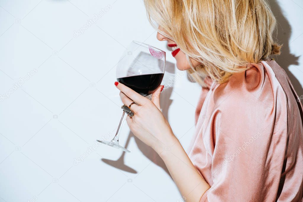 Portrait of pretty blonde Caucasian woman holding glass of red wine.