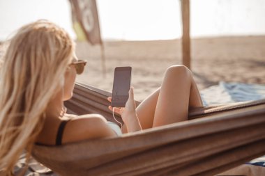 Hamak beach ve cep telefonunu yazarak yatan oldukça beyaz kadın.