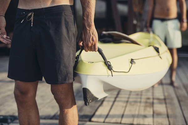 Two unrecognisable men carrying a canoe on wooden deck.