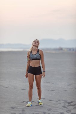 Güzel sporcumuz kumlu plaj ve stratching boynunu ayakta.