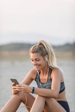 Kumsalda oturuyor ve cep telefonunu tutan oldukça beyaz sporcumuz.