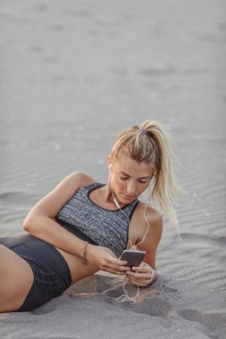 Kumsalda oturuyor ve cep telefonunu tutan oldukça beyaz sporcumuz.