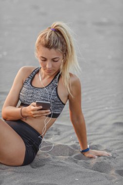 Kumsalda oturuyor ve cep telefonunu tutan oldukça beyaz sporcumuz.