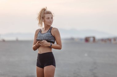 Kumsalda duran ve cep telefonunu tutan güzel beyaz kadın runner.