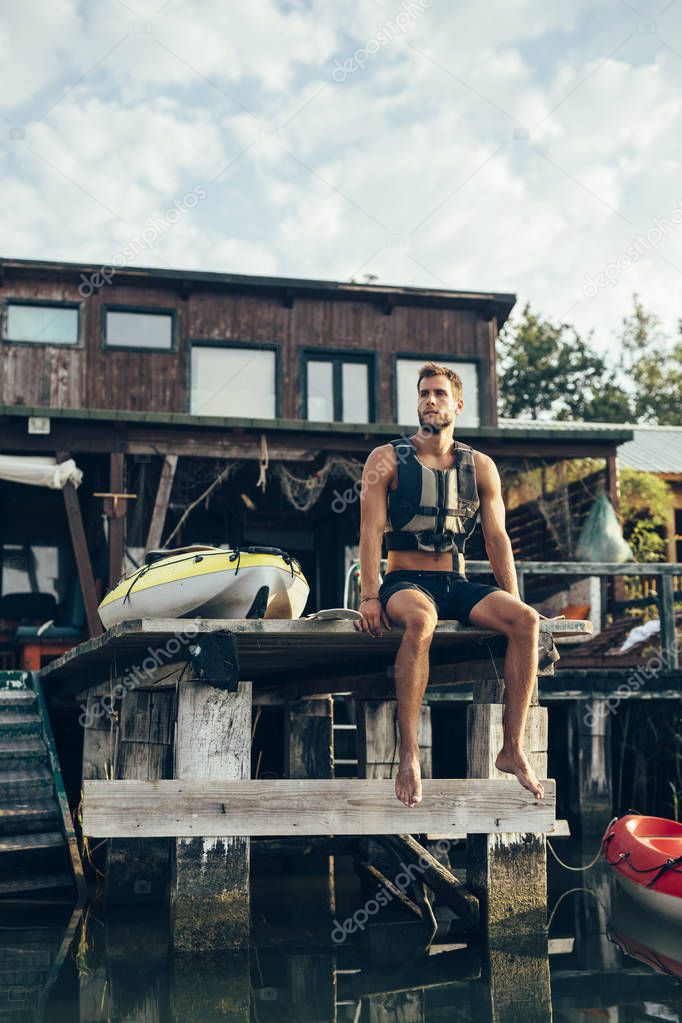 Handsome Caucasian sportsman kayaker sitting on wooden deck by the river.