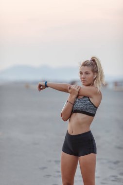 Güzel sporcumuz kumlu plaj ve stratching kolunu ayakta.