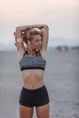 Güzel sporcumuz kumlu plaj ve stratching kolunu ayakta.