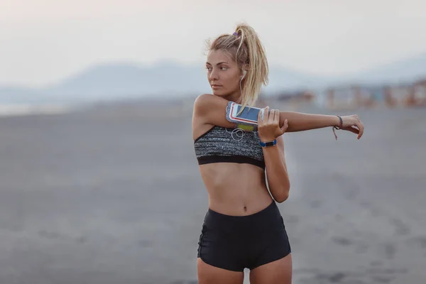 美丽的运动员站在沙滩上 Stratching 她的手臂 — 图库照片