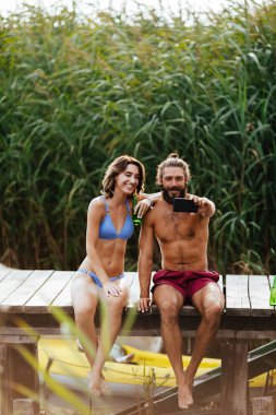 Genç adam ve cep telefonu kamera ile selfie alarak ve yaz Nehri üzerinde zevk kadın.