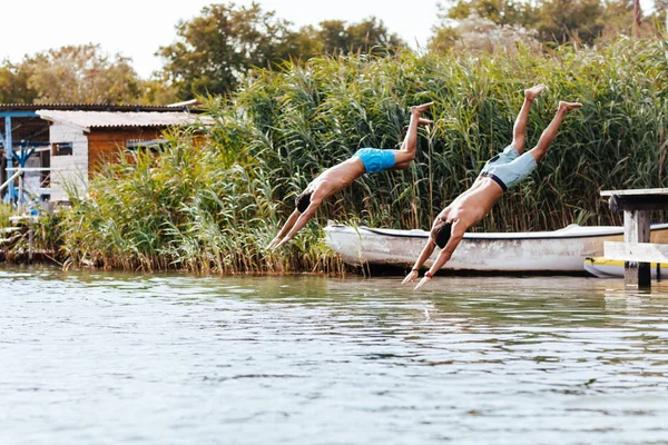 Young men jumping in river from wooden deck.