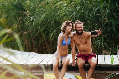 Genç adam ve cep telefonu kamera ile selfie alarak ve yaz Nehri üzerinde zevk kadın.