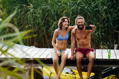 Genç adam ve cep telefonu kamera ile selfie alarak ve yaz Nehri üzerinde zevk kadın.